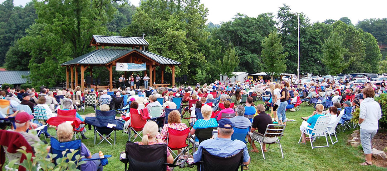 people in lawn chairs at outdoor concert with bandstand